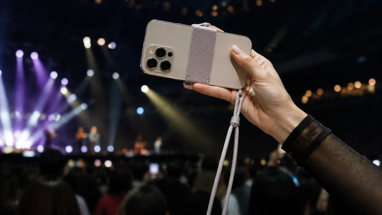A hand holding a smartphone that has a wide elastic strap across the back and a lanyard cord